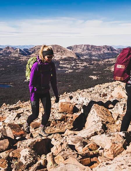 Two women hiking uphill through rocky terrain.