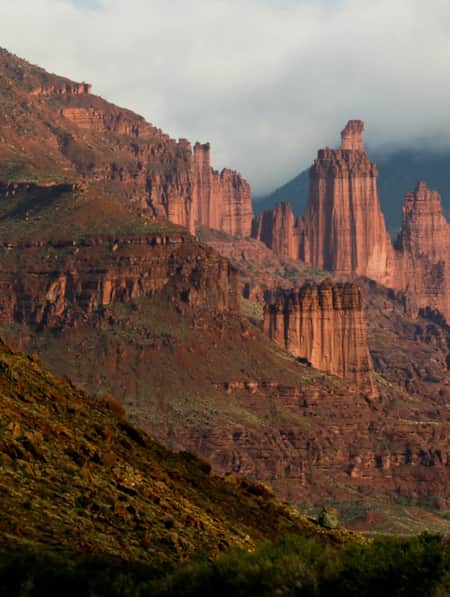 Tall red rock tower formations surrounded by mountains and clouds.