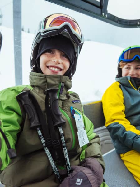 Two young boys wearing winter ski gear inside an enclosed gondola.