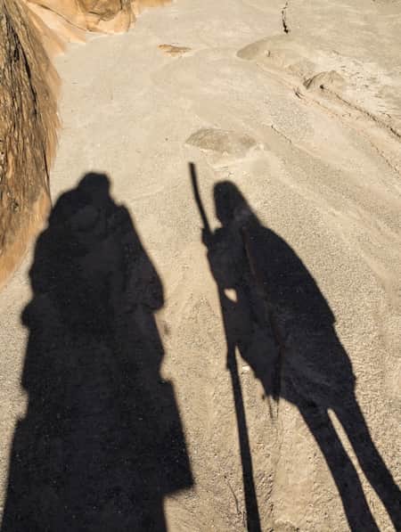 Shadows of two people hiking on a trail.