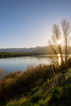 A sunrise over mountains with a lake in the foreground, surrounded by green hills.