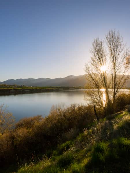 A sunrise over mountains with a lake in the foreground, surrounded by green hills.