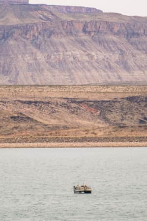 Two people on a pontoon boat in a lake, with bare mountains in the backdrop.