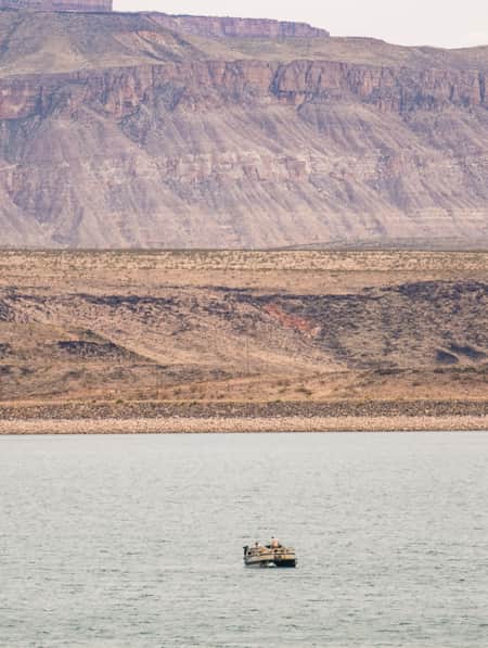 Two people on a pontoon boat in a lake, with bare mountains in the backdrop.