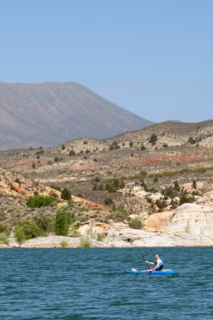 Two people paddle boarding on a lake, with hills and mountains in the background.