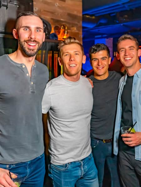 Four men standing together in a bar, smiling and looking at the camera.