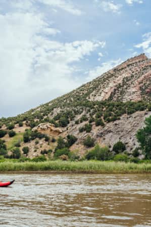 A person kayaking on a river in front of a slanted rock formation that tapers to a point.