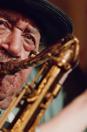 A man playing the saxophone with another man behind him singing into a microphone.