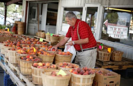 A man hand-picking peaches from circular wooden baskets at a farm stand.