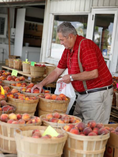 A man hand-picking peaches from circular wooden baskets at a farm stand.