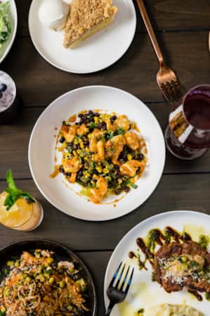 An aerial shot of dishes arranged on a table, including roasted carrots, pie, steak, salad, and biscuits.