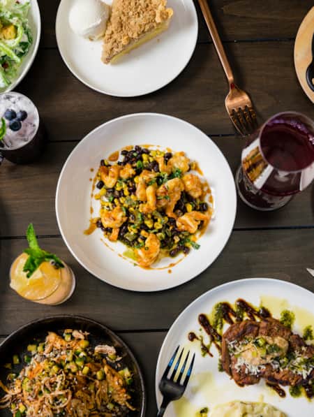 An aerial shot of dishes arranged on a table, including roasted carrots, pie, steak, salad, and biscuits.