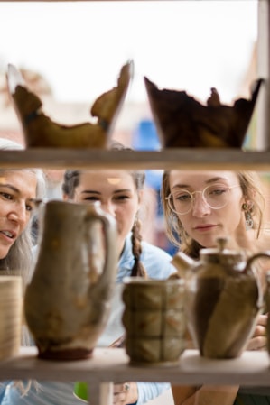 Three women looking at shelves of pottery through a window.