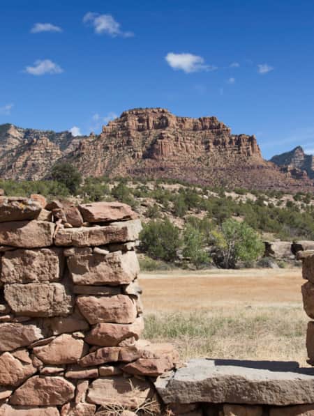 A wall made from many rocks with a cut-out, set in front of a distant mountain range.