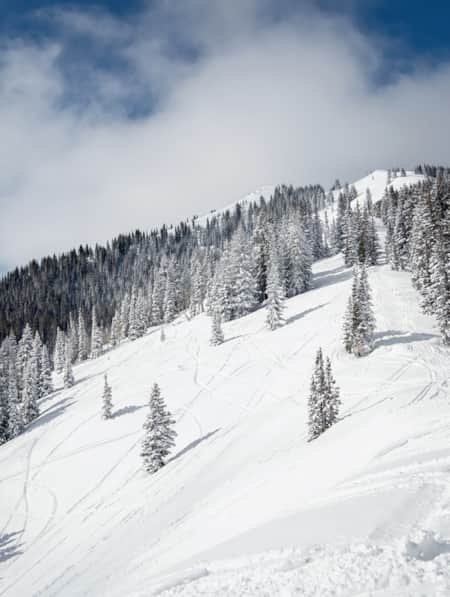 The ridge of a snow-covered mountain with two snowmobile riders traveling along it.