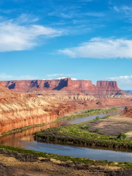 An expansive view of red rock monuments with a river flowing through.