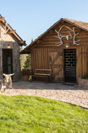 Two buildings, one made of logs and the other with a rock exterior, built close together and sharing a courtyard.