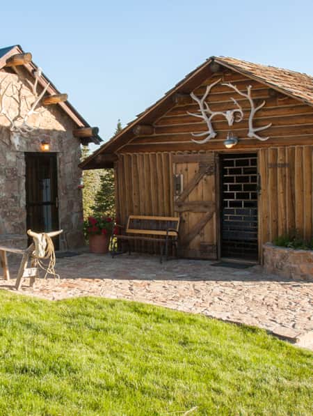 Two buildings, one made of logs and the other with a rock exterior, built close together and sharing a courtyard.