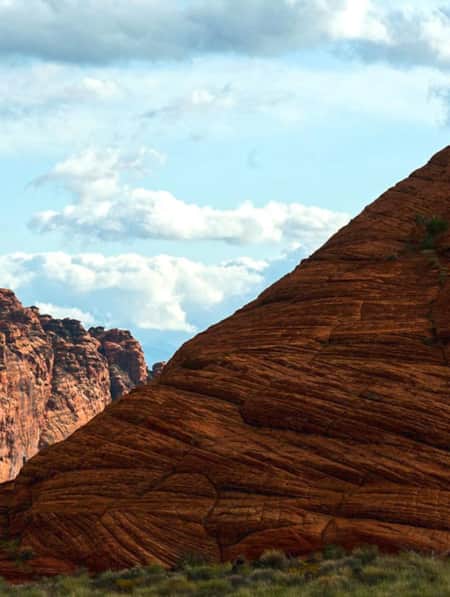 The silhouettes of two people at the top of a large red mountain during the day.
