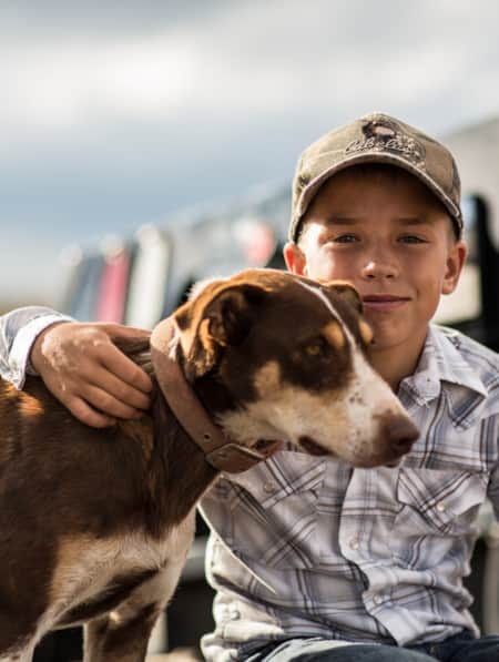A young boy with his arm around a dog standing beside him.