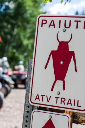 A trail sign reading 'Paiute Trail ATV' with ATVs visible in the background.
