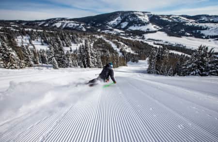A skier making a big turn on a freshly groomed run, leaning into the turn.
