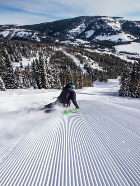 A skier making a big turn on a freshly groomed run, leaning into the turn.