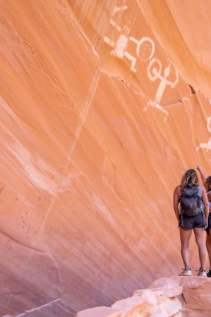 Two women looking up at petroglyphs on a large, flat rock wall.
