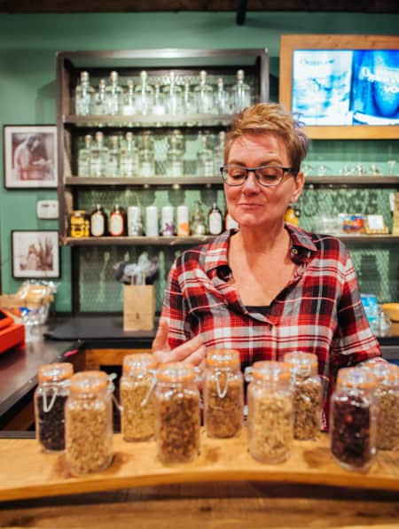 A woman standing behind a display of small glass jars filled with spices.