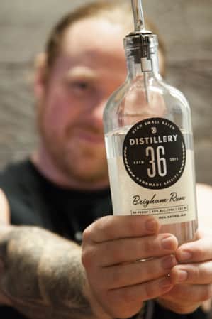 A man holding the bottom of a glass bottle with both hands, with a label that reads 'Rum 36 Brighman Rum.'