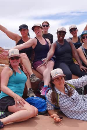 A group of women in hiking clothing posing for a photo with one another, set against a red rock slab.