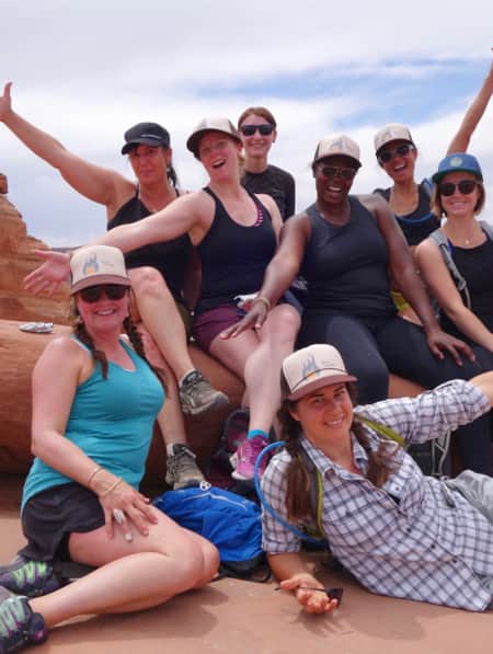 A group of women in hiking clothing posing for a photo with one another, set against a red rock slab.