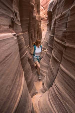 A woman hiking through a narrow slot canyon.