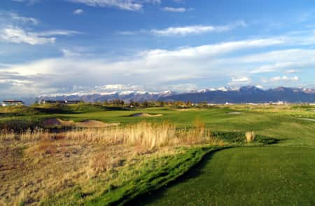 A golf course with mountains in the backdrop and houses on a hill overlooking the course.