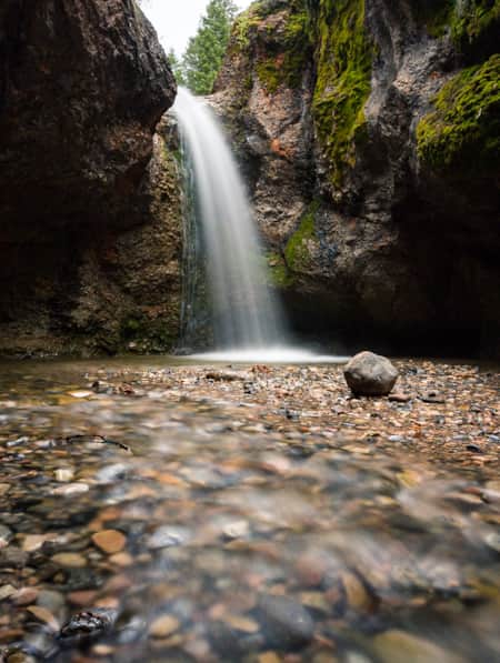 A tall waterfall starting at an opening in the ground and cascading into a deep hole below.