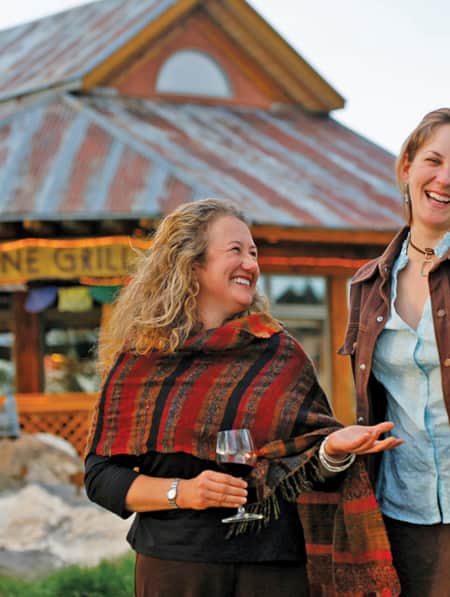 Two women facing the camera, candidly smiling in front of a restaurant.