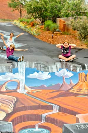Women and children posing around a three-dimensional chalk painting on the ground.