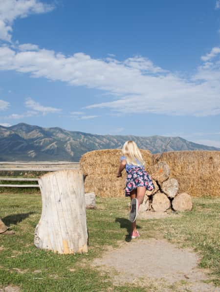 Young girl throwing an axe for target shooting to a bails of hay with a man in wearing traditional western clothing.