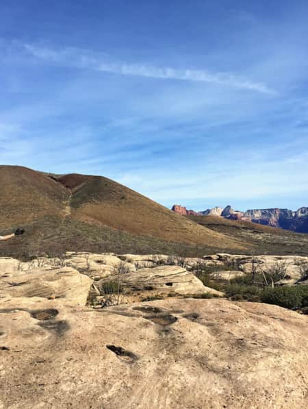 Mountain biker resting on the seat of their bike in Gooseberry Mesa, with their hands in the air and smiling.