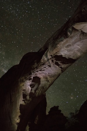 The underside view of a natural rock arch against a starry night sky.