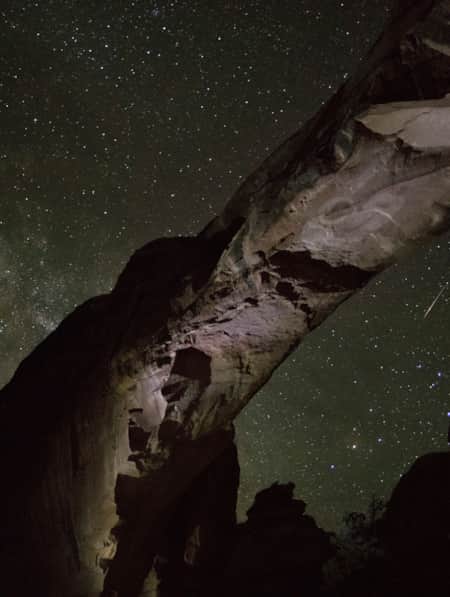 The underside view of a natural rock arch against a starry night sky.