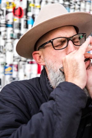 A man playing the harmonica in front of a metal wall covered in stickers.