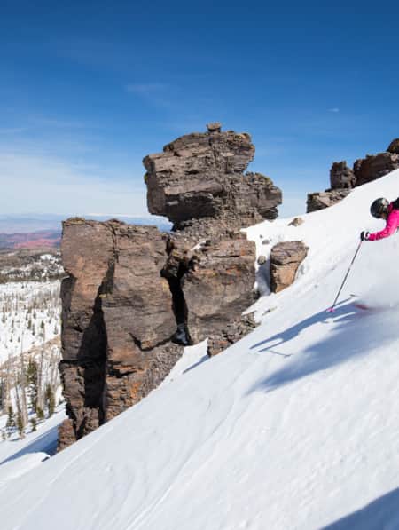 A skier making first tracks down a mountain, surrounded by scattered rocks and trees