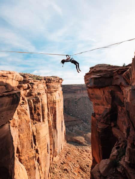 A woman harnessed to a rope, pulling herself across a canyon on a rope secured to each side.