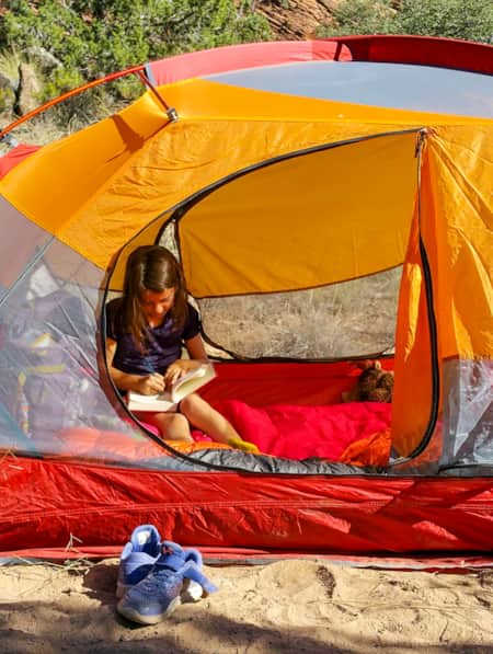 A young child inside a tent, writing in a book.