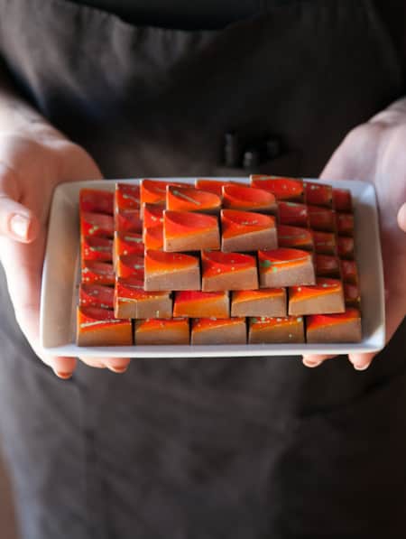 A person holding a white rectangular plate of chocolates, with each morsel adorned with an orange decorative glaze.