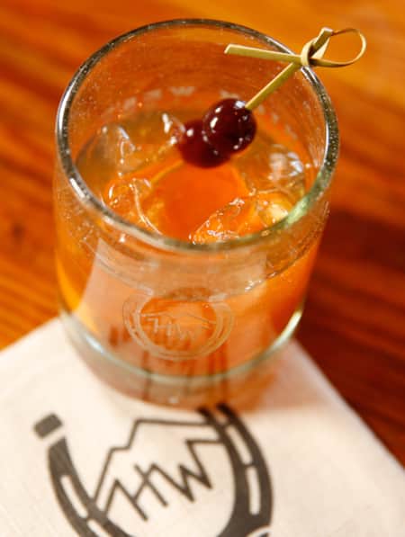 A small glass filled with a mixed drink, topped with a toothpick of cherries, resting on a white napkin.