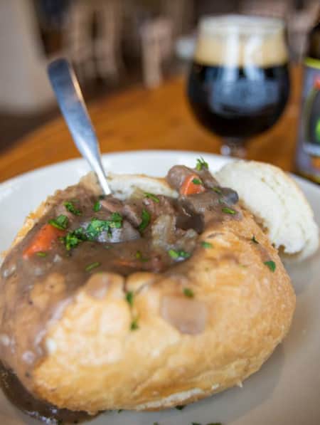 A bread bowl filled with beef stew, accompanied by a dark beer on the side.