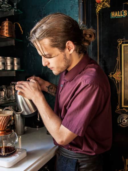 A barista in a speakeasy setting preparing a pour-over coffee.