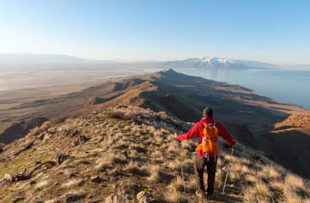 A hiker walking along the ridge of a grassy mountain top.
